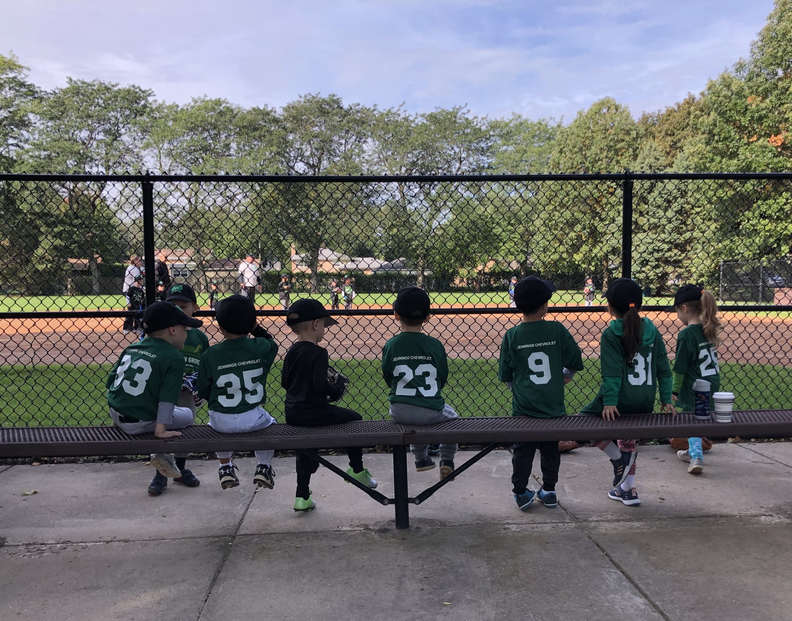 Kids sitting on a baseball bench waiting for tee ball